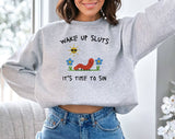 "Wake Up Sluts, It's Time To Sin" design on an ash gray unisex crewneck sweatshirt