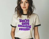 "You're Doing Amazing Sweetie" design on a natural ringer t-shirt with black contrast trim