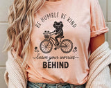 "Be Humble Be Kind Frog Bicycle" design on a peach unisex t-shirt