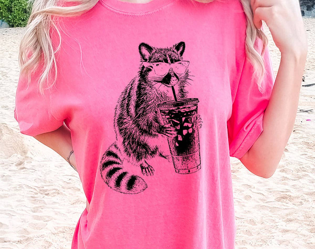 "Raccoon Drinking Iced Coffee" design on a pink watermelon Comfort Colors t-shirt