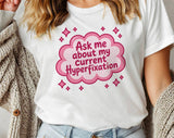 "Ask Me About My Current Hyperfixation" design on a white unisex t-shirt