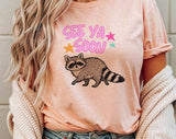 "See You Soon Raccoon" design on a peach unisex t-shirt