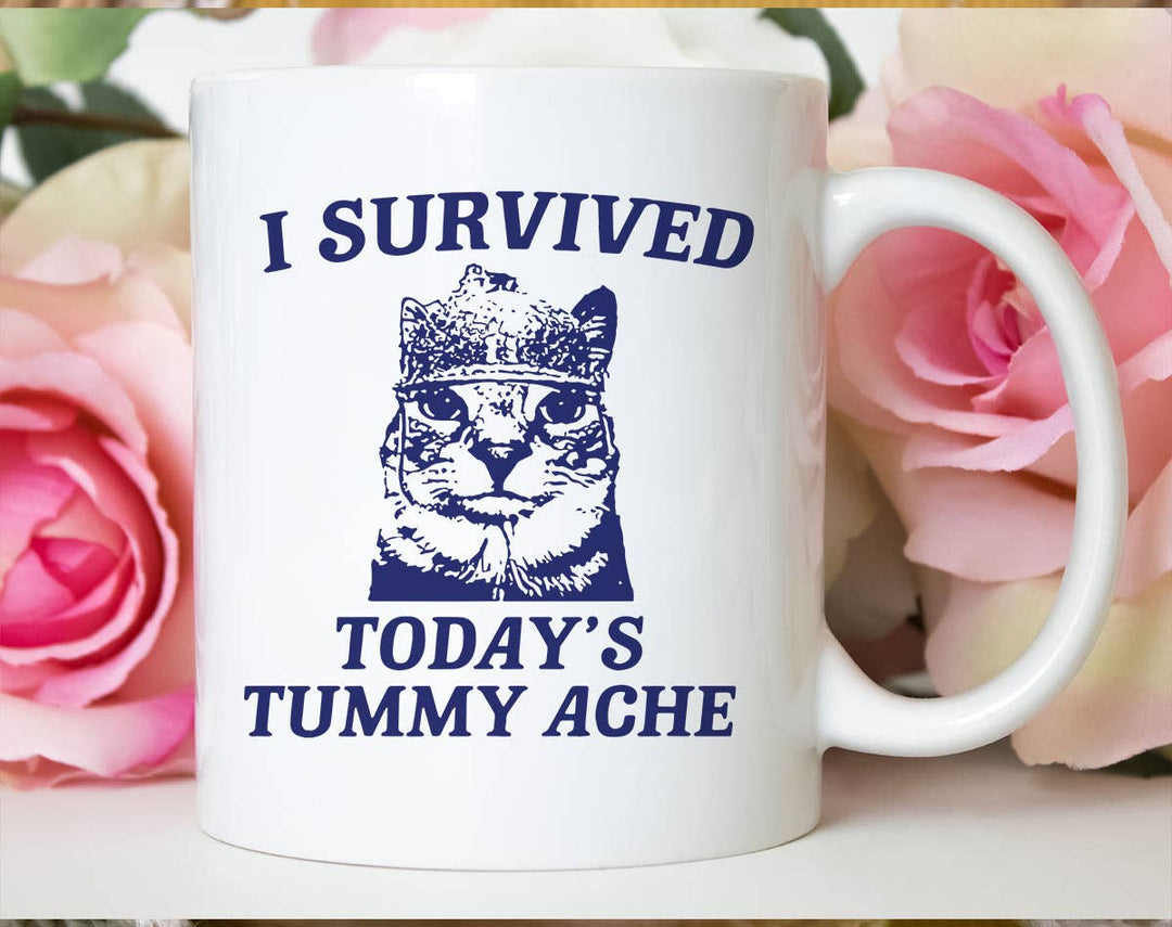 "I Survived Todays Tummy Ache" design on a white ceramic coffee mug