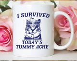 "I Survived Todays Tummy Ache" design on a white ceramic coffee mug