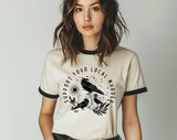 "Support Your Local Murder Crow" design on a natural ringer t-shirt with black contrast trim