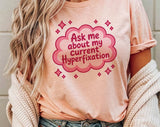 "Ask Me About My Current Hyperfixation" design on a peach unisex t-shirt