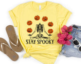 "Stay Spooky Skeleton Juggle" design on a pale yellow unisex t-shirt