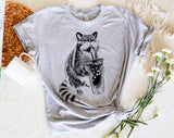 "Raccoon Drinking Iced Coffee" design on a heather gray unisex t-shirt