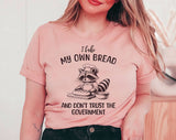 "I Bake Bread & Don't Trust The Government Raccoon" design on a peach unisex t-shirt