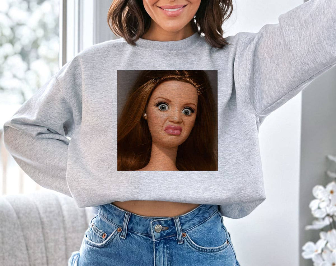 "Disgusted Doll Face" design on an ash gray unisex crewneck sweatshirt
