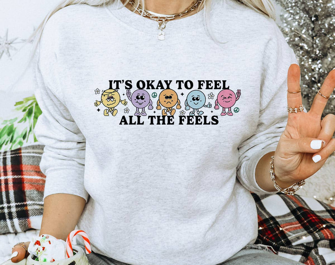 "It's Okay To Feel All The Feels" design on an ash gray unisex crewneck sweatshirt