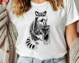 "Raccoon Drinking Iced Coffee" design on a white unisex t-shirt