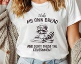 "I Bake Bread & Don't Trust The Government Raccoon" design on a white unisex t-shirt