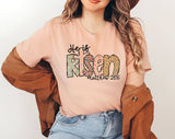 "He Is Risen Matthew 28:6" design on a peach unisex t-shirt
