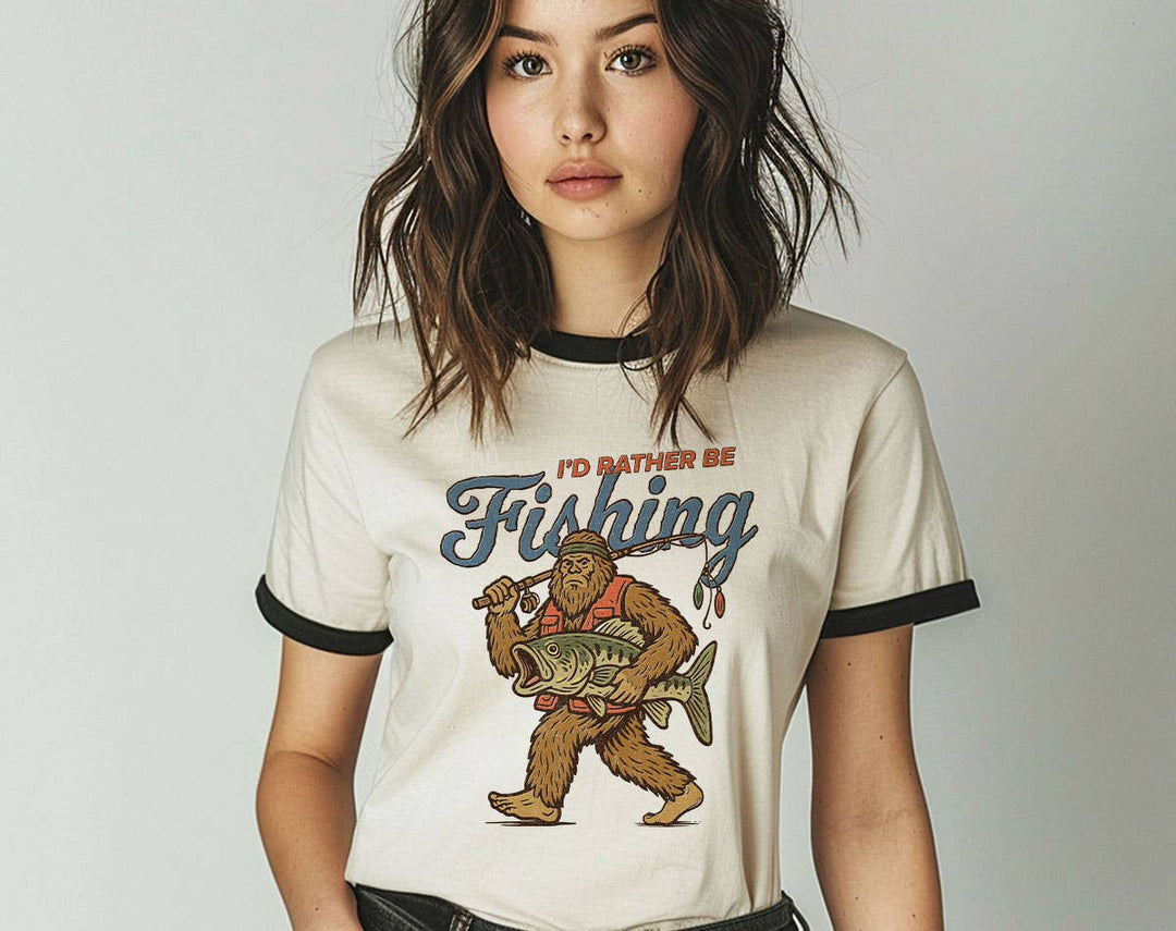 "I'd Rather Be Fishing Bigfoot" design on a natural ringer t-shirt with black contrast trim