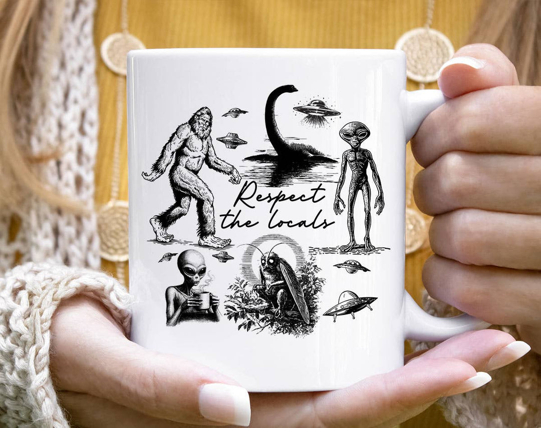 "Respect The Locals Mothman Bigfoot Ufo Alien" design on a white ceramic coffee mug